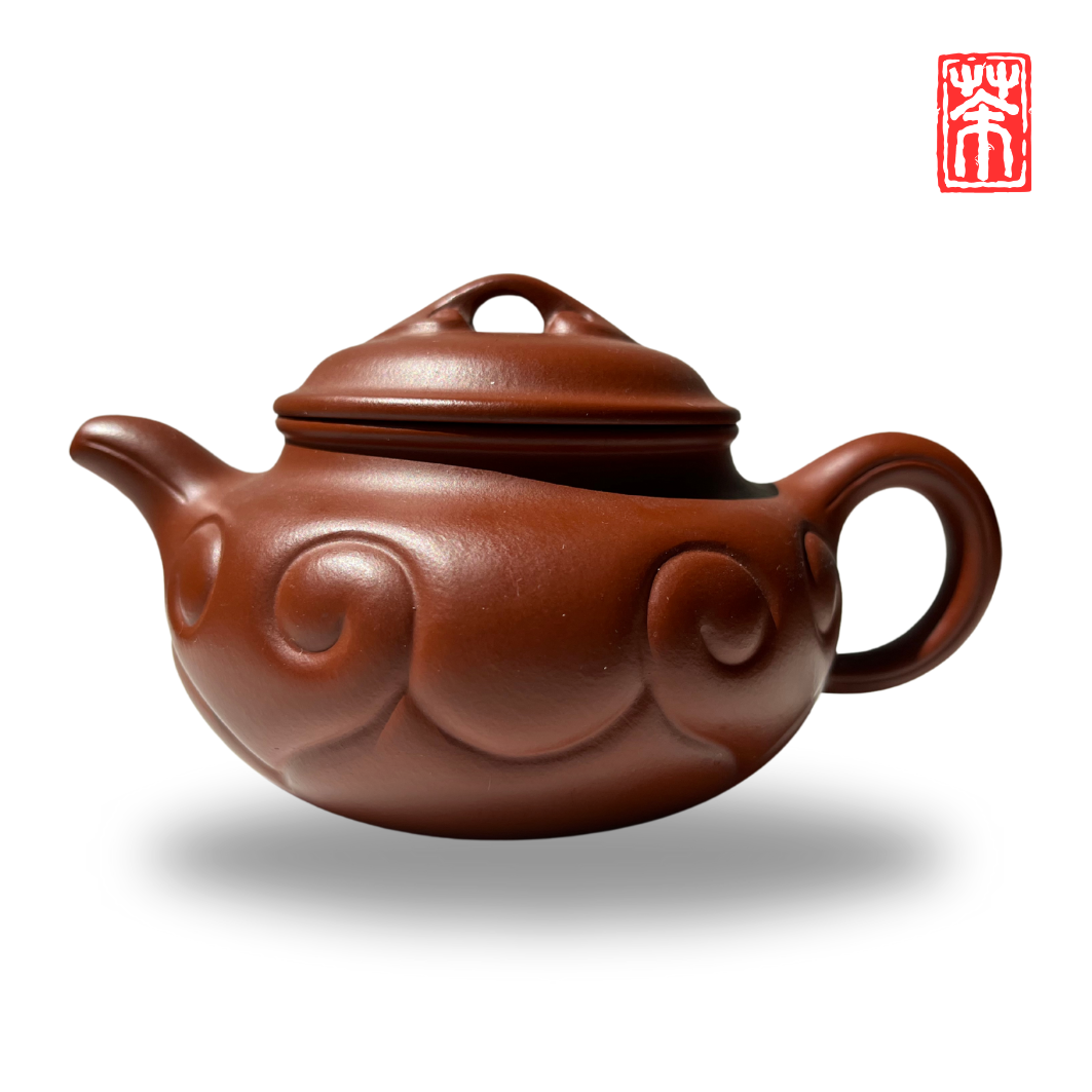 Ergänzen Sie Ihre Teekollektion mit dieser eleganten Yixing Teekanne aus rötlichem Zisha-Ton. Die lebendige, helle Tonfarbe und das kunstvoll eingearbeitete Wolkenrelief machen sie zum Blickfang – perfekt, um die erdigen Aromen von Pu-Erh und dunklen Tees stilvoll zu genießen.