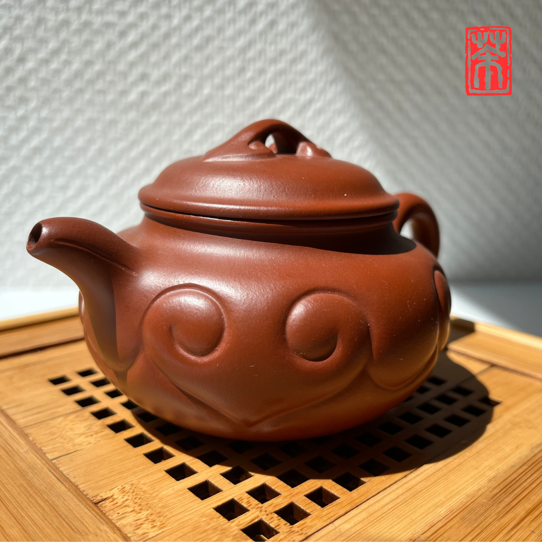 Ergänzen Sie Ihre Teekollektion mit dieser eleganten Yixing-Teekanne aus rötlichem Zisha-Ton. Die lebendige, helle Tonfarbe und das kunstvoll eingearbeitete Wolkenrelief machen sie zum Blickfang – perfekt, um die erdigen Aromen von Pu-Erh und dunklen Tees stilvoll zu genießen.